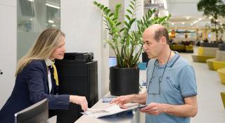 Medewerker onthaal AZ Sint-Maarten toont een patiëntenbrochure aan een patiënt in de zorgboulevard van het ziekenhuis